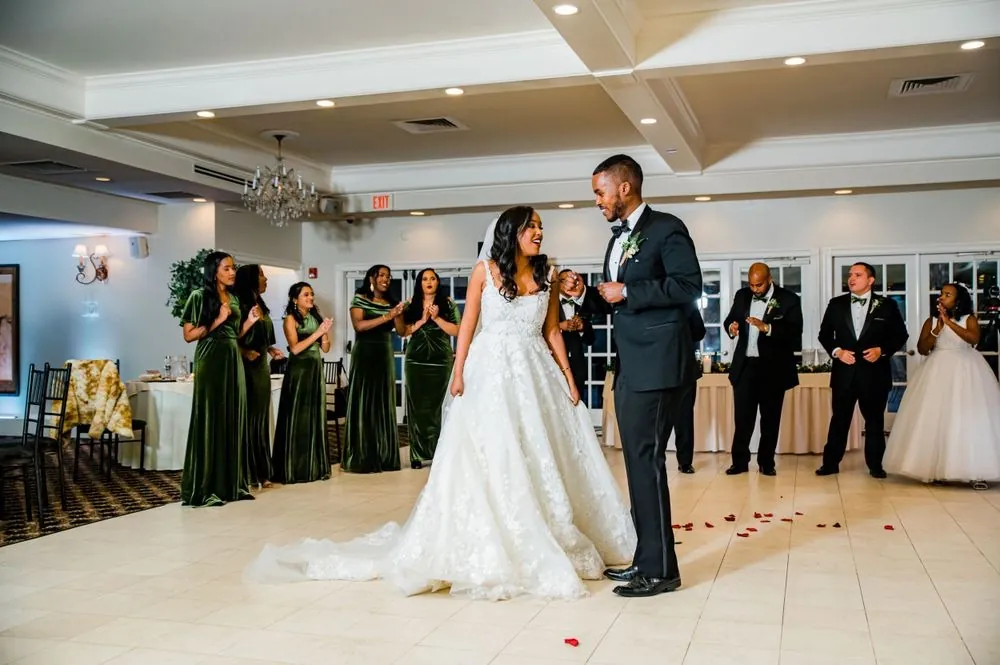 The couple dances across a floor scattered with red petals as the wedding party claps