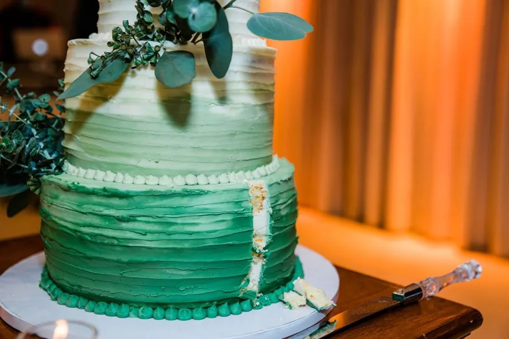 An ombre green cake with gold leaf and eucalyptus on a wooden stand