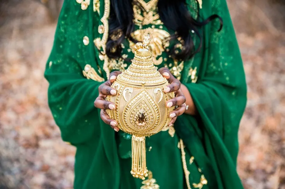 Close view of an ornate gold vessel held against emerald embroidered fabric