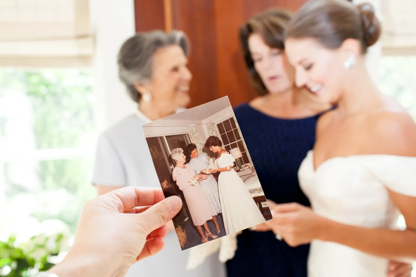 An old wedding snapshot held up in front of the bride and 2 smiling women