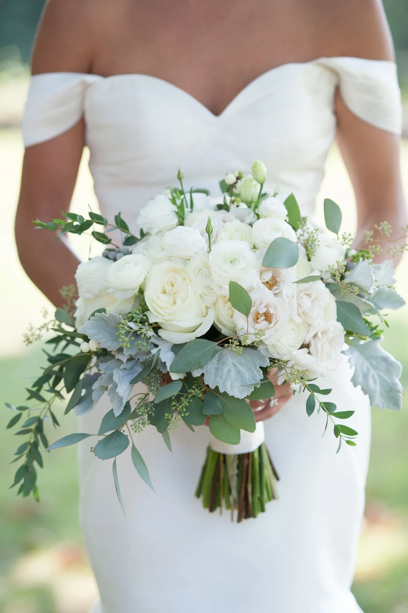 The bride holds a bouquet of white roses and silvery eucalyptus against her gown