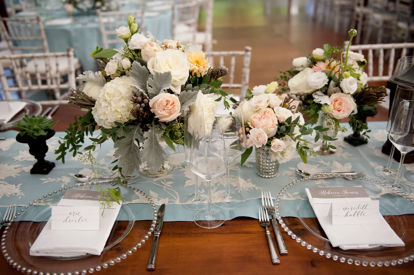Blush roses, candles, and beaded chargers on a pale blue table runner