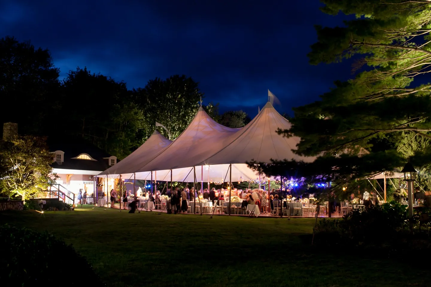 The sailcloth tent glows among dark trees on the lawn at night