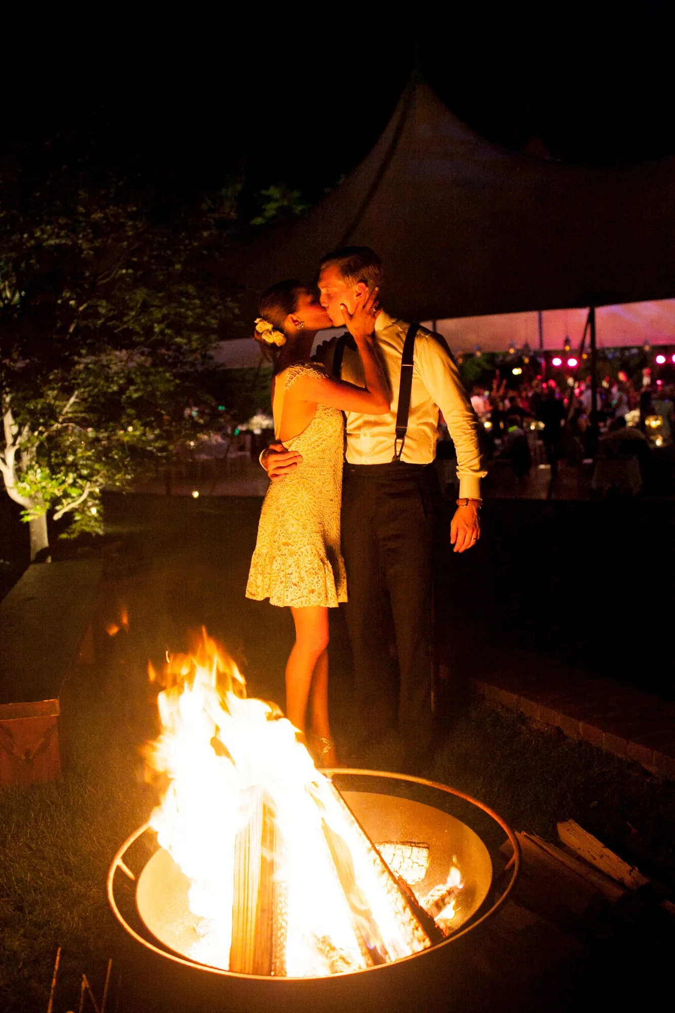 A guest stands beside a crackling fire pit on the lawn after dark
