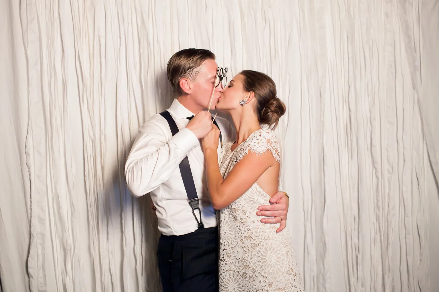 Becca and James share a kiss against a draped white photo booth backdrop
