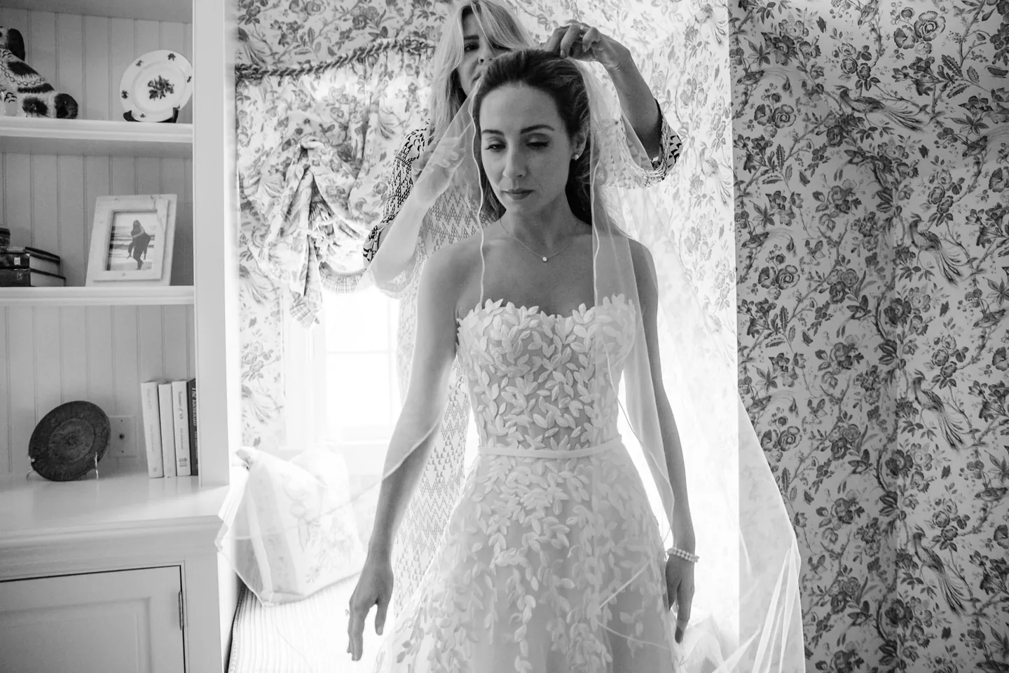 Black and white frame of the bride in a strapless lace gown by a patterned window