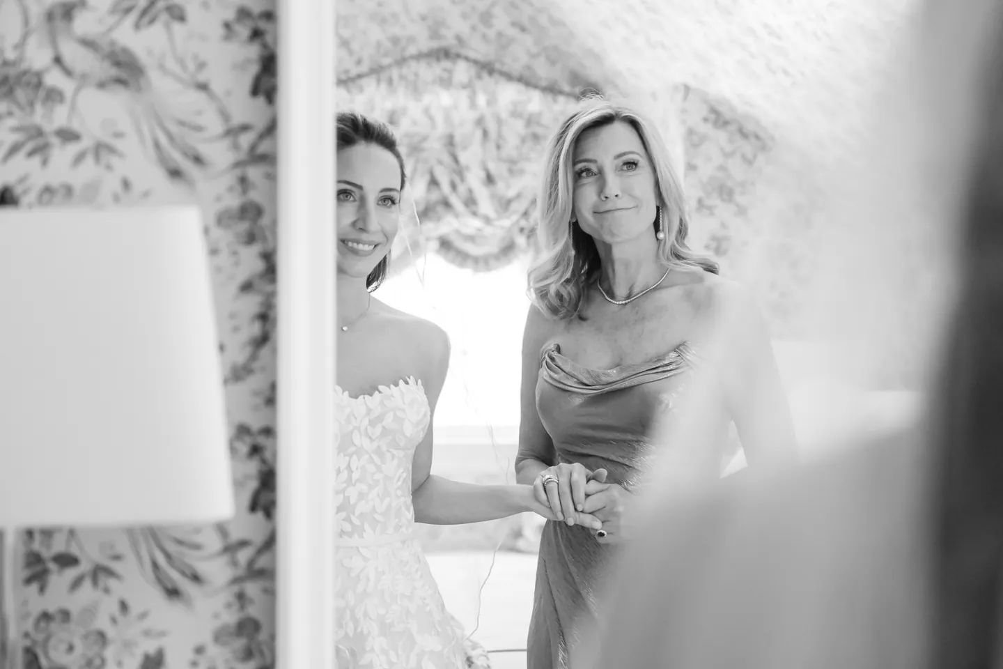 Black and white frame of a woman watching from the doorway as the bride finishes dressing