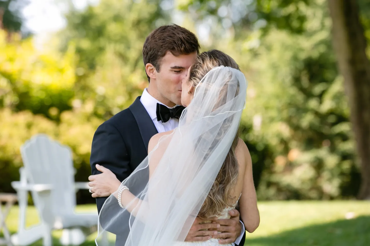 Britt and Andrew kiss under green trees, her veil lifting in the breeze