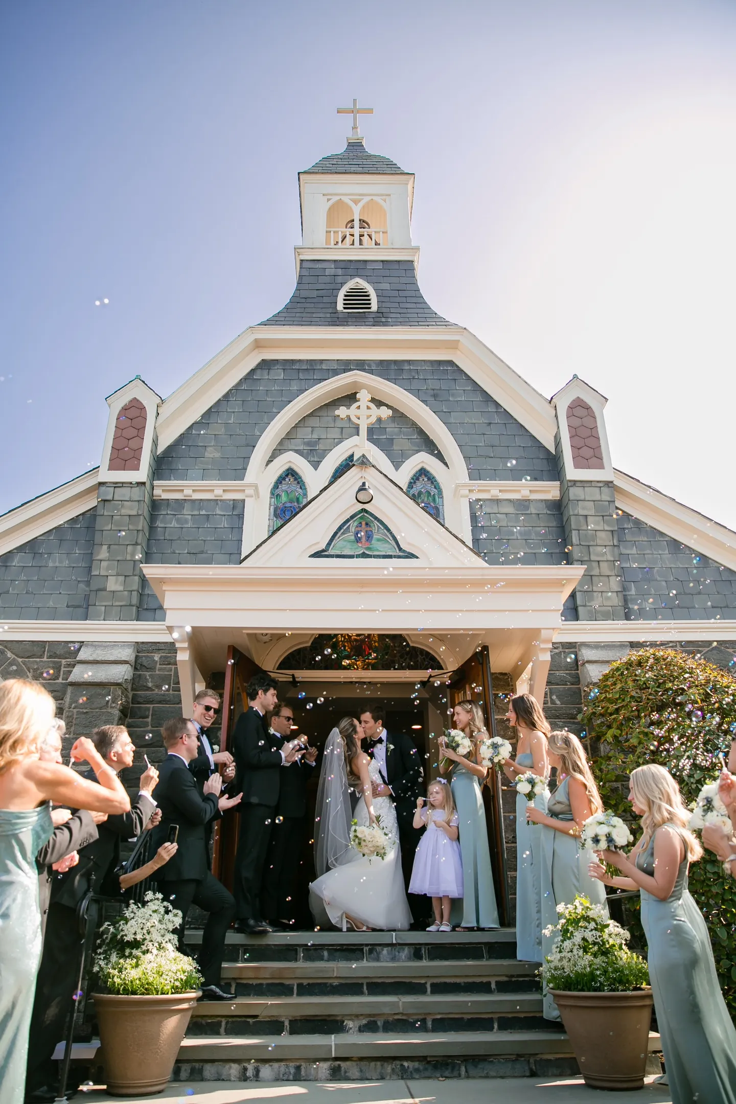 Guests toss petals as the couple leave a grey shingled chapel topped with a white cupola
