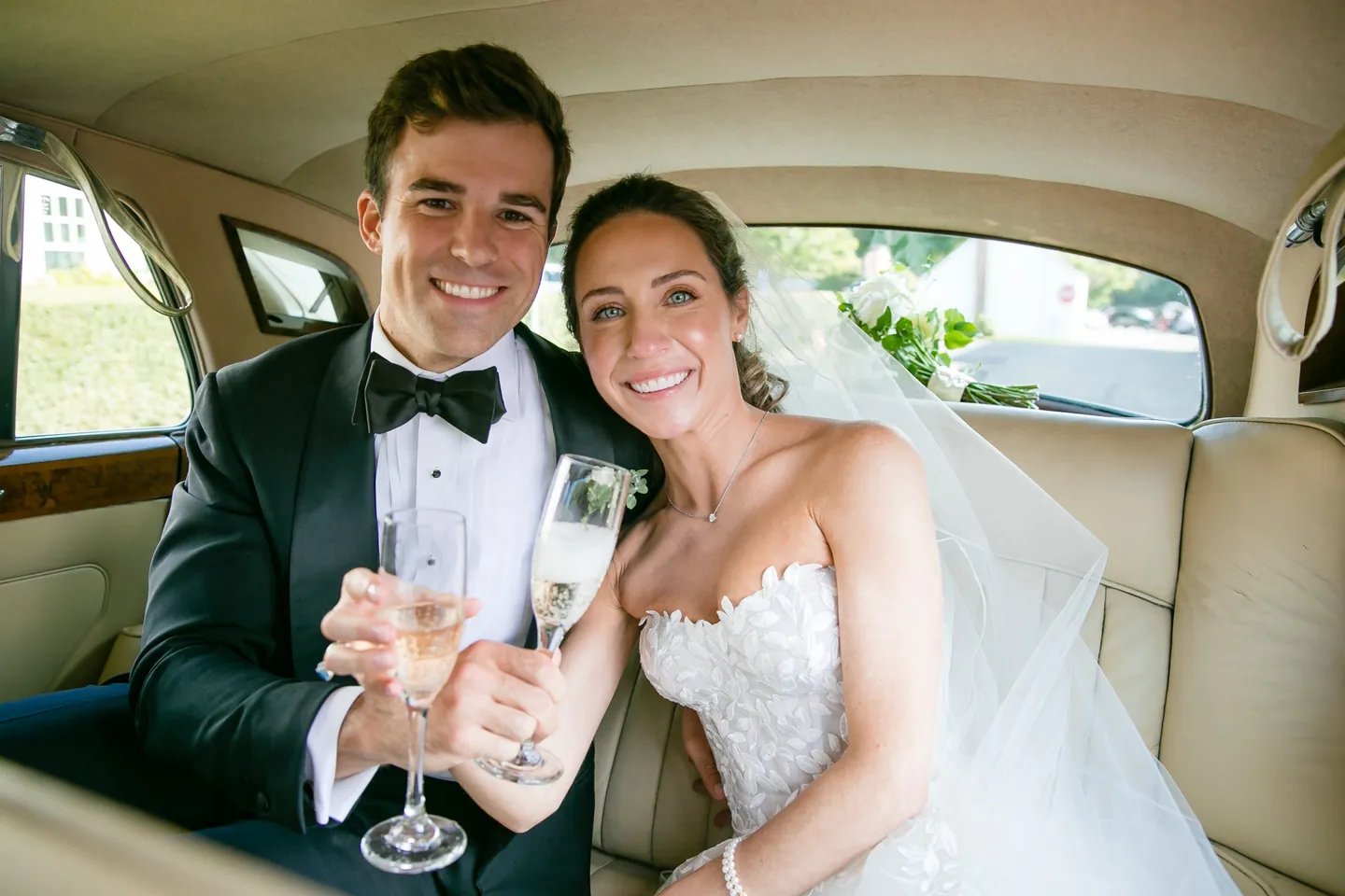 Britt and Andrew raise champagne flutes in the back seat of a vintage car