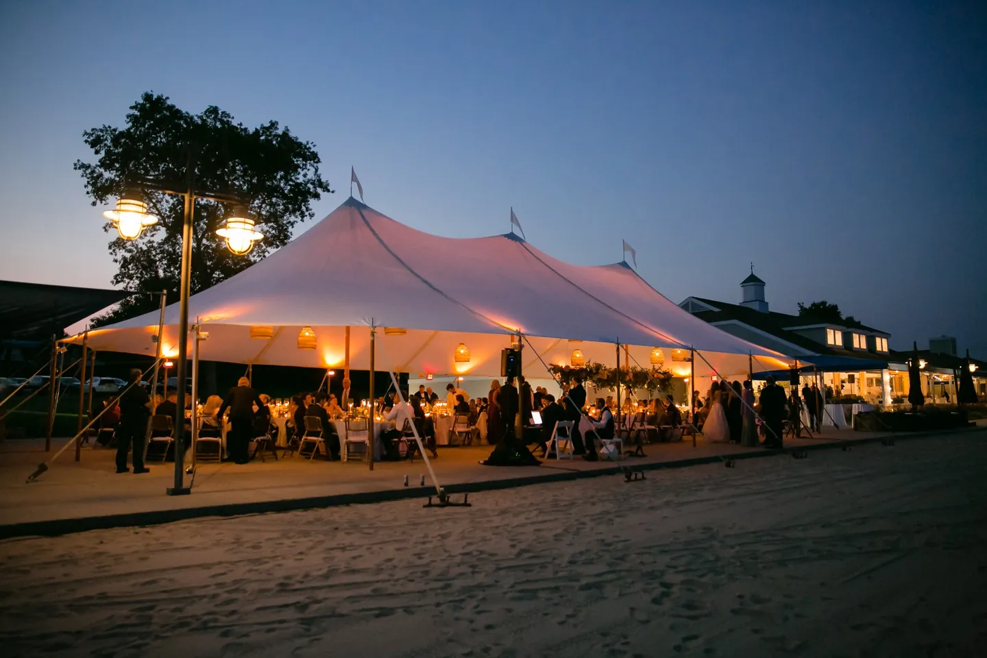The sailcloth tent glows warm on the beach under a deep blue evening sky