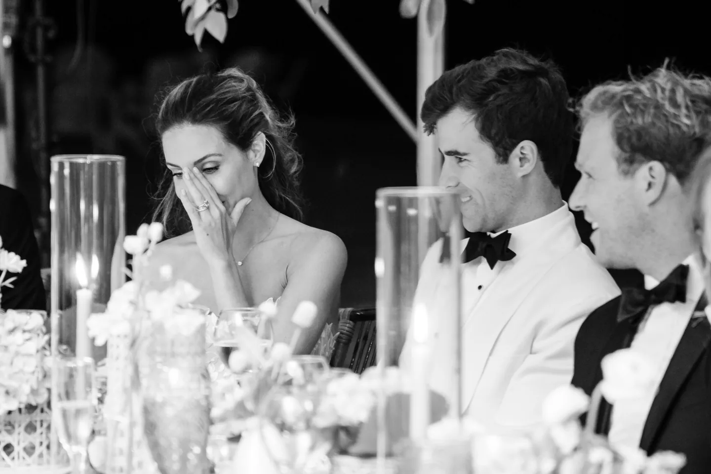 Black and white frame of the bride covering her face with laughter during toasts