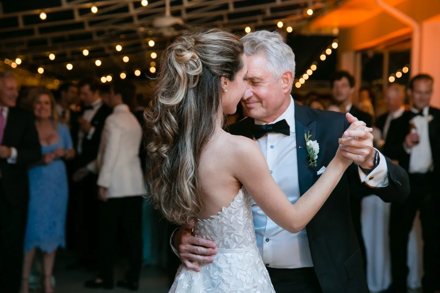 The bride dances cheek to cheek with an older man under string lights