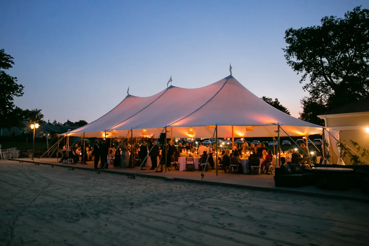 Wide view of the lit sailcloth tent at twilight with trees silhouetted behind