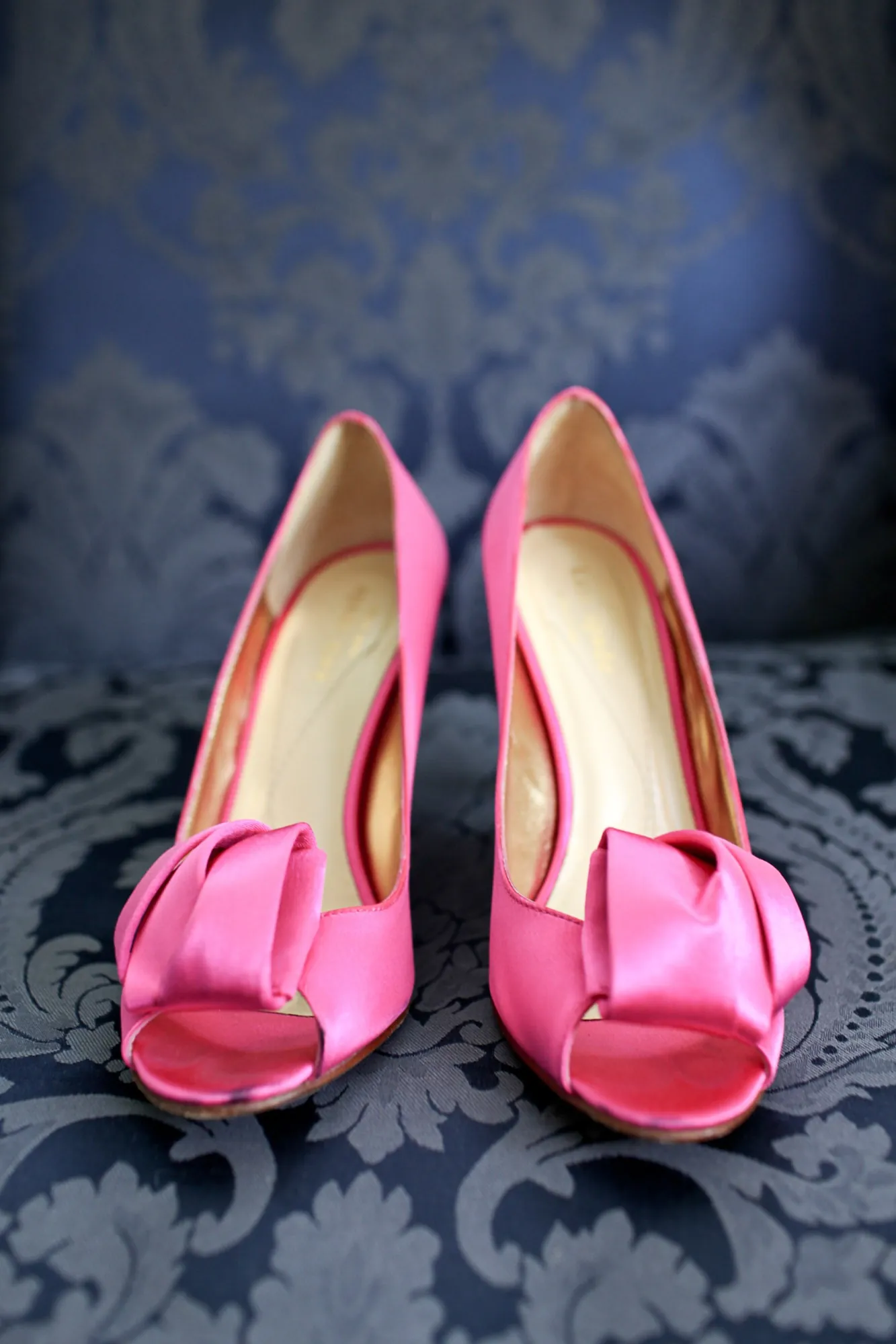 Hot pink satin heels rest on a navy damask chair