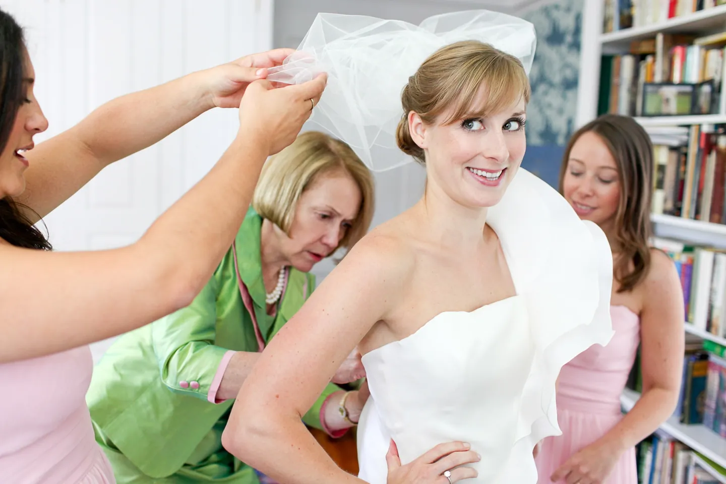 Women help settle the bride's veil in a room lined with bookshelves