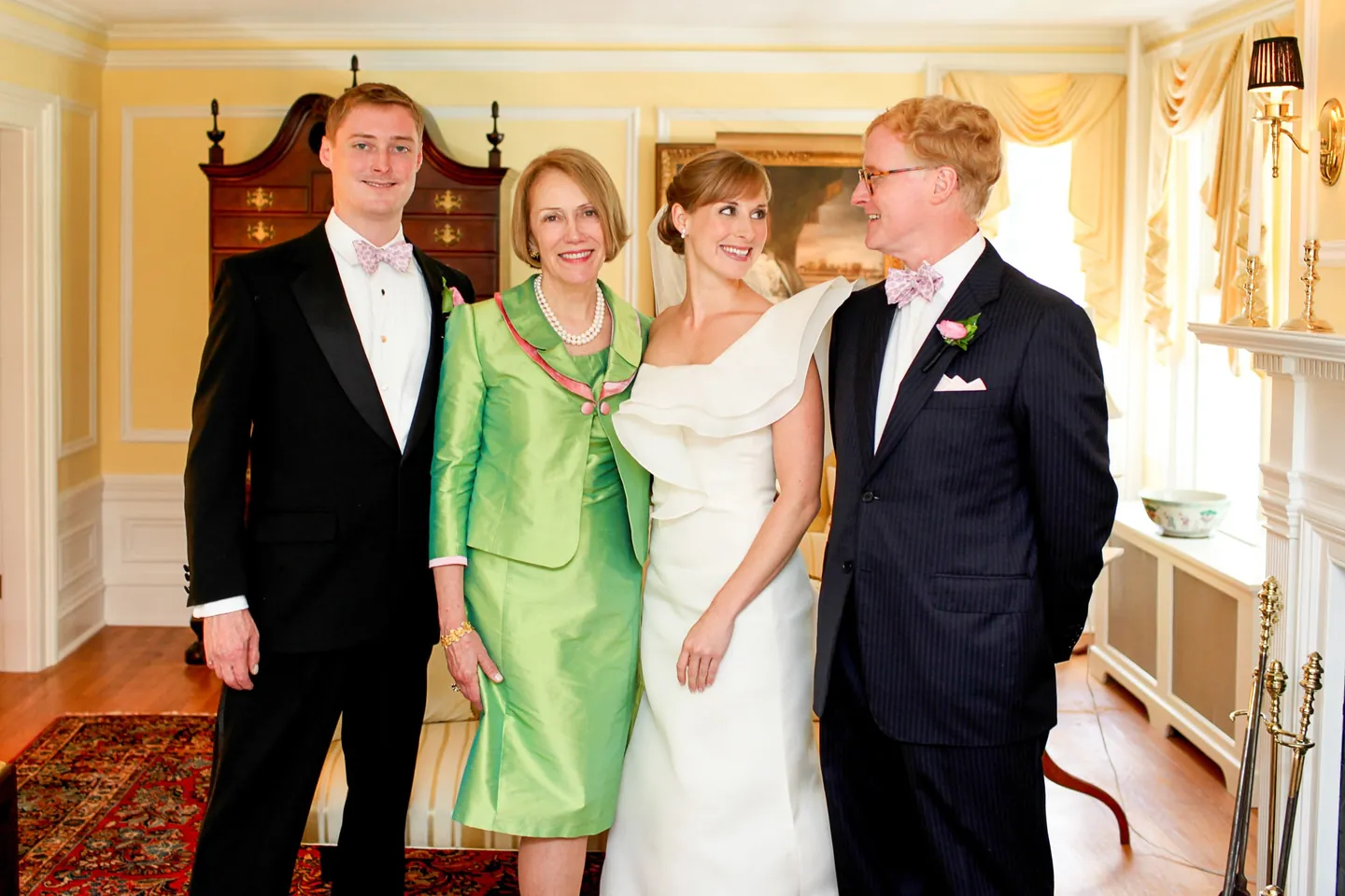 The bride stands with family in black tie and green silk in a paneled room