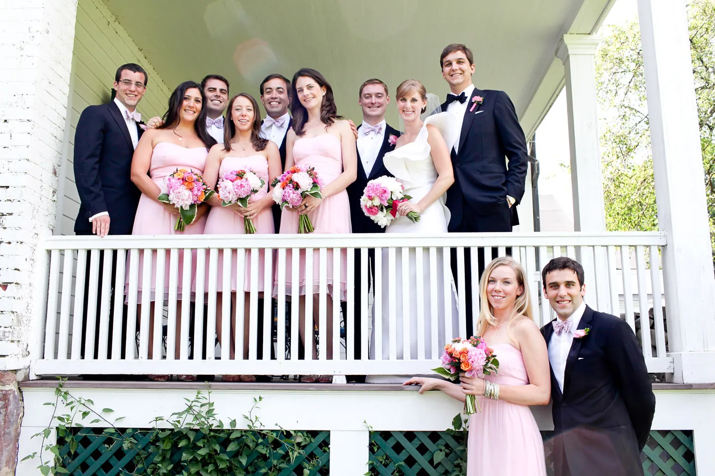 The wedding party in pink dresses and black tie crowds onto a white porch