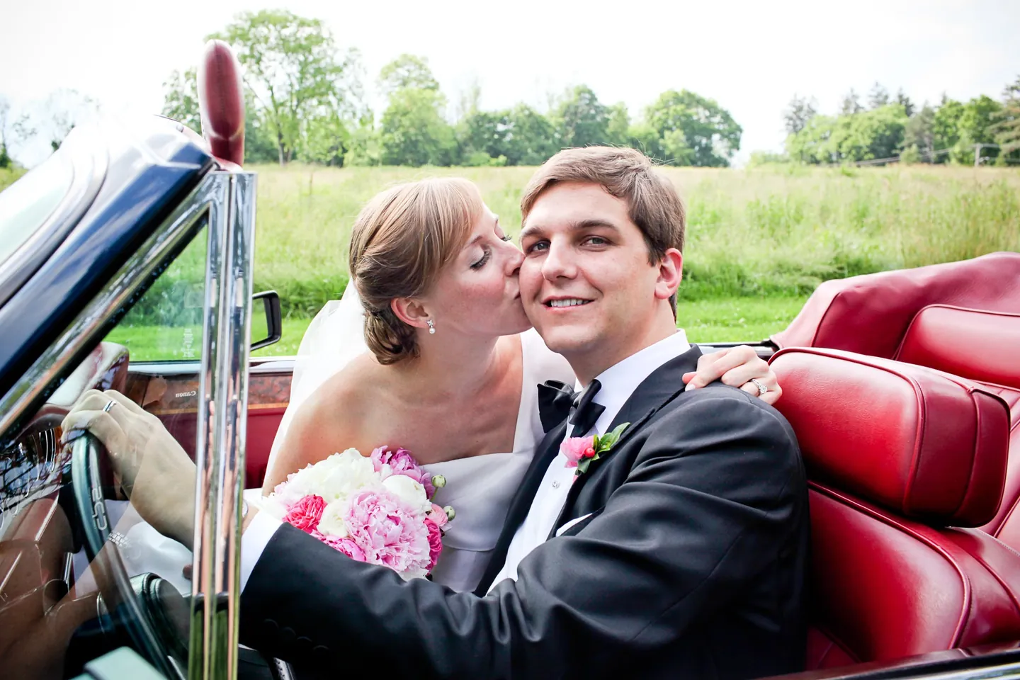 Caity kisses Matt's cheek in the red leather seats of the convertible