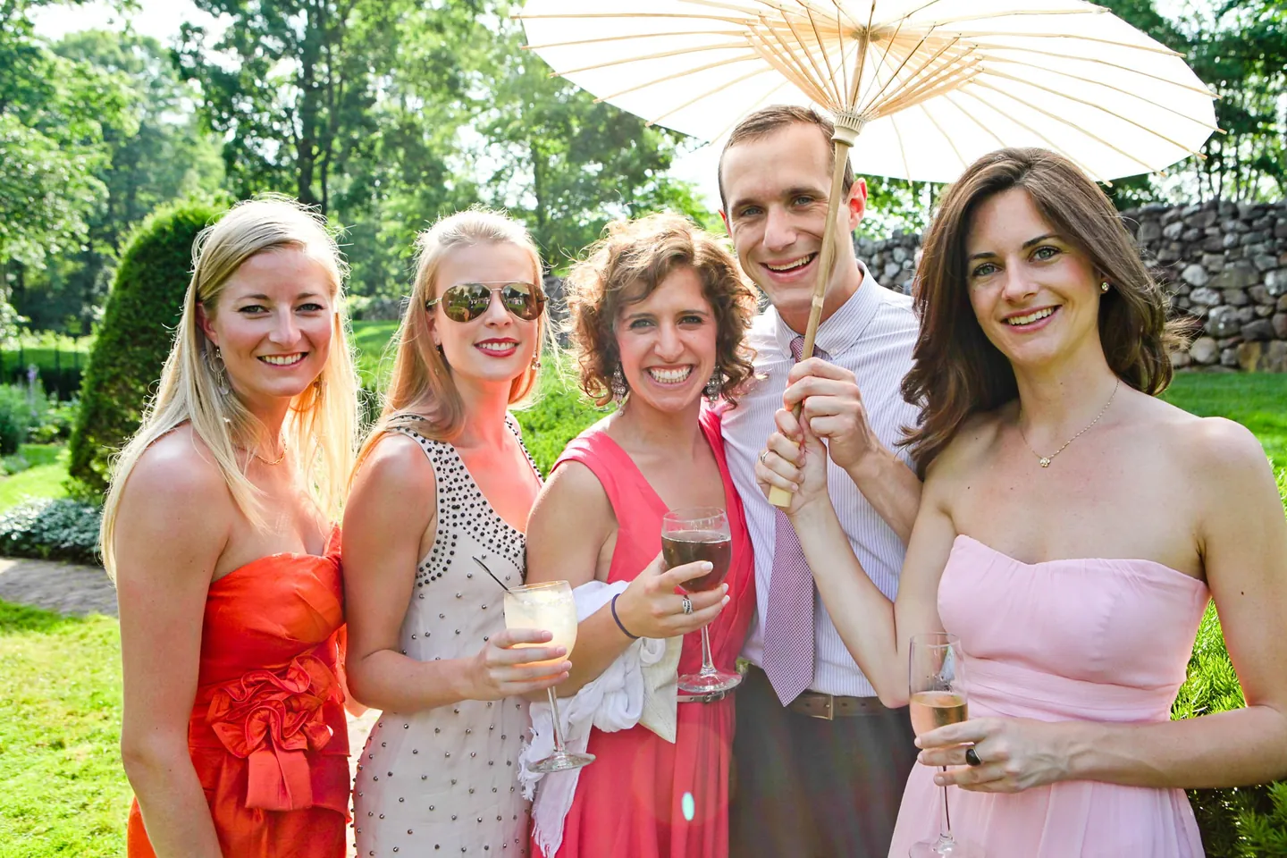 Friends with paper parasols raise glasses in the garden during cocktail hour