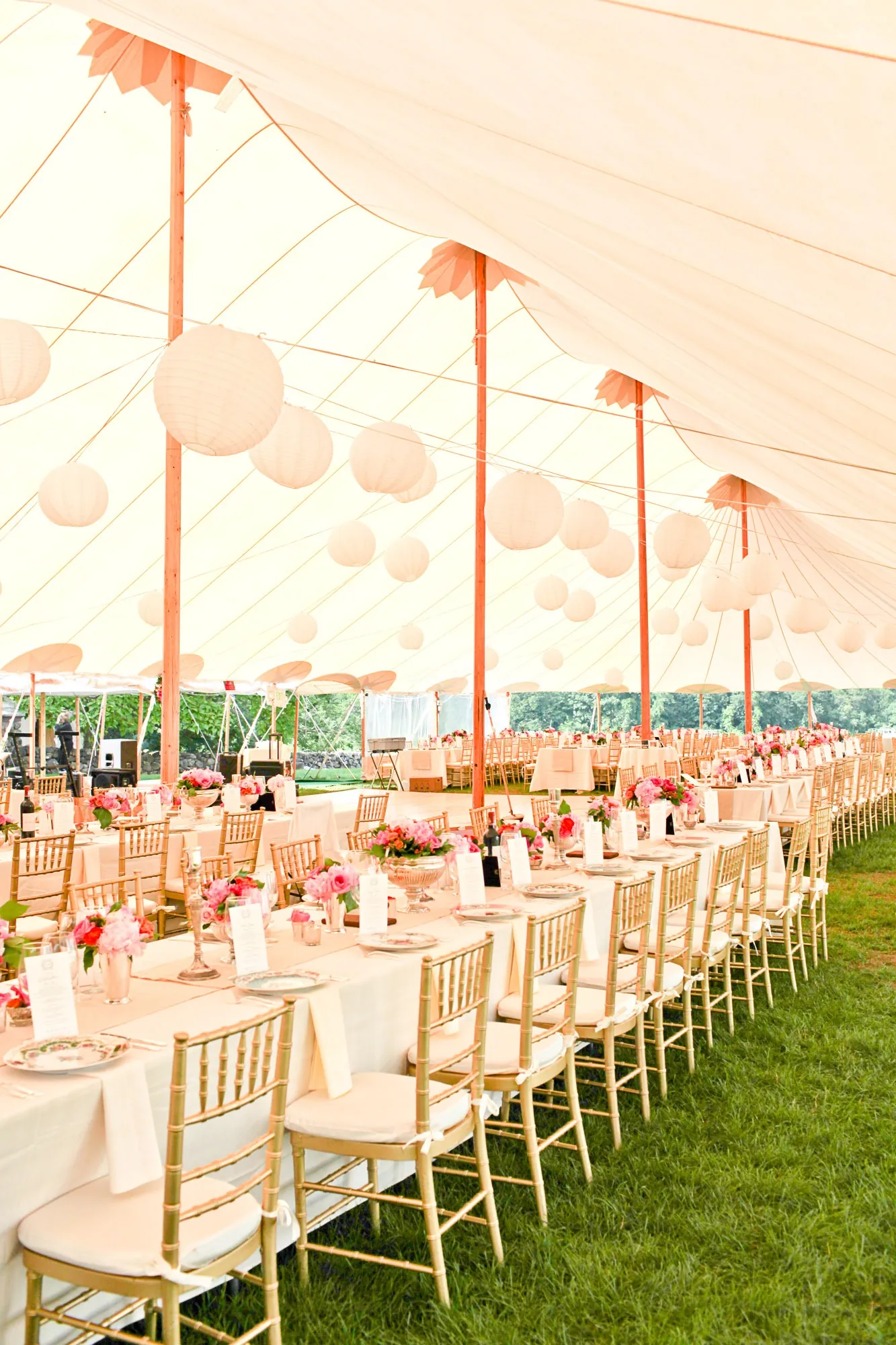 Long tables with gold chairs run beneath paper lanterns inside the sailcloth tent