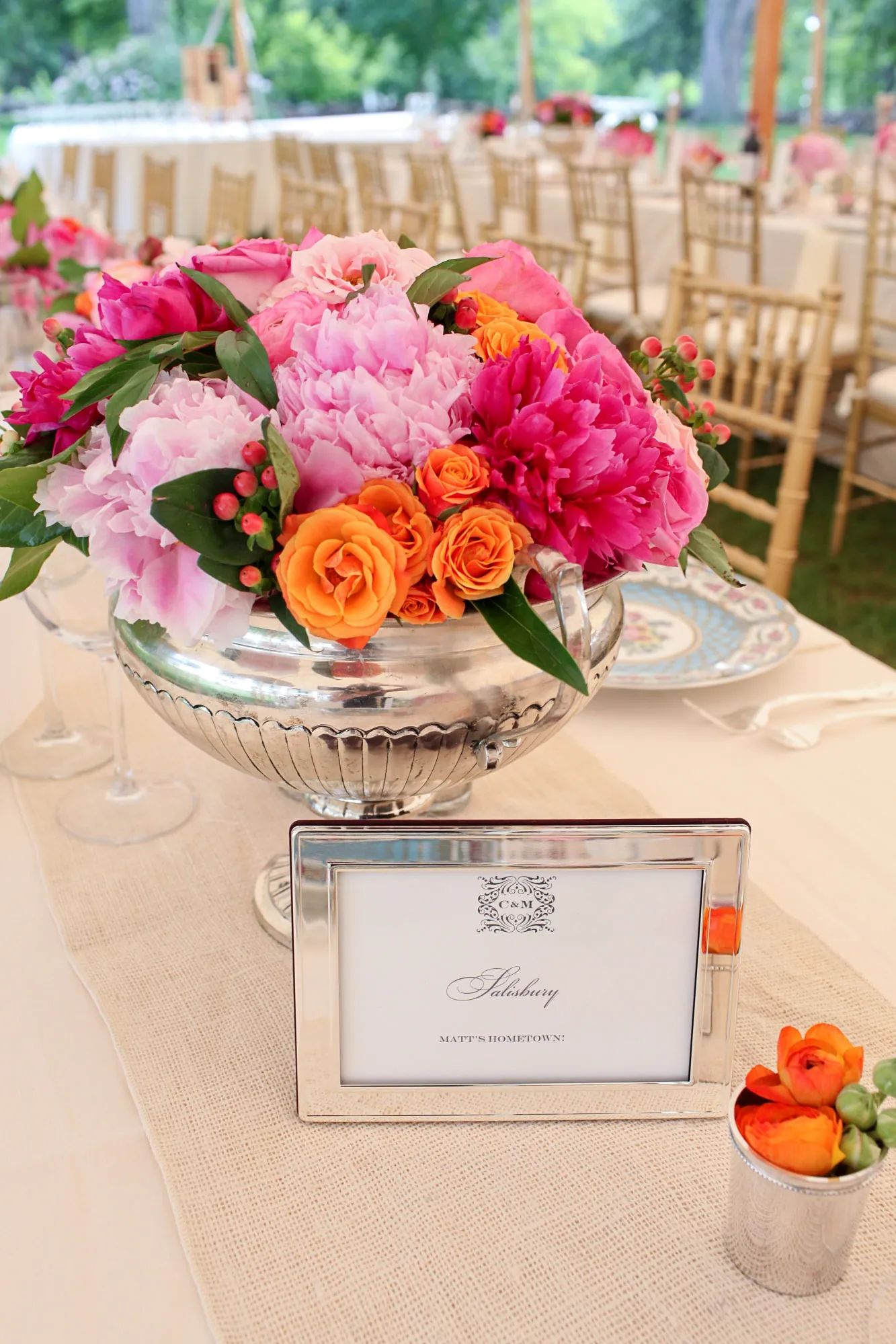A silver bowl of pink and orange peonies and roses beside a table number