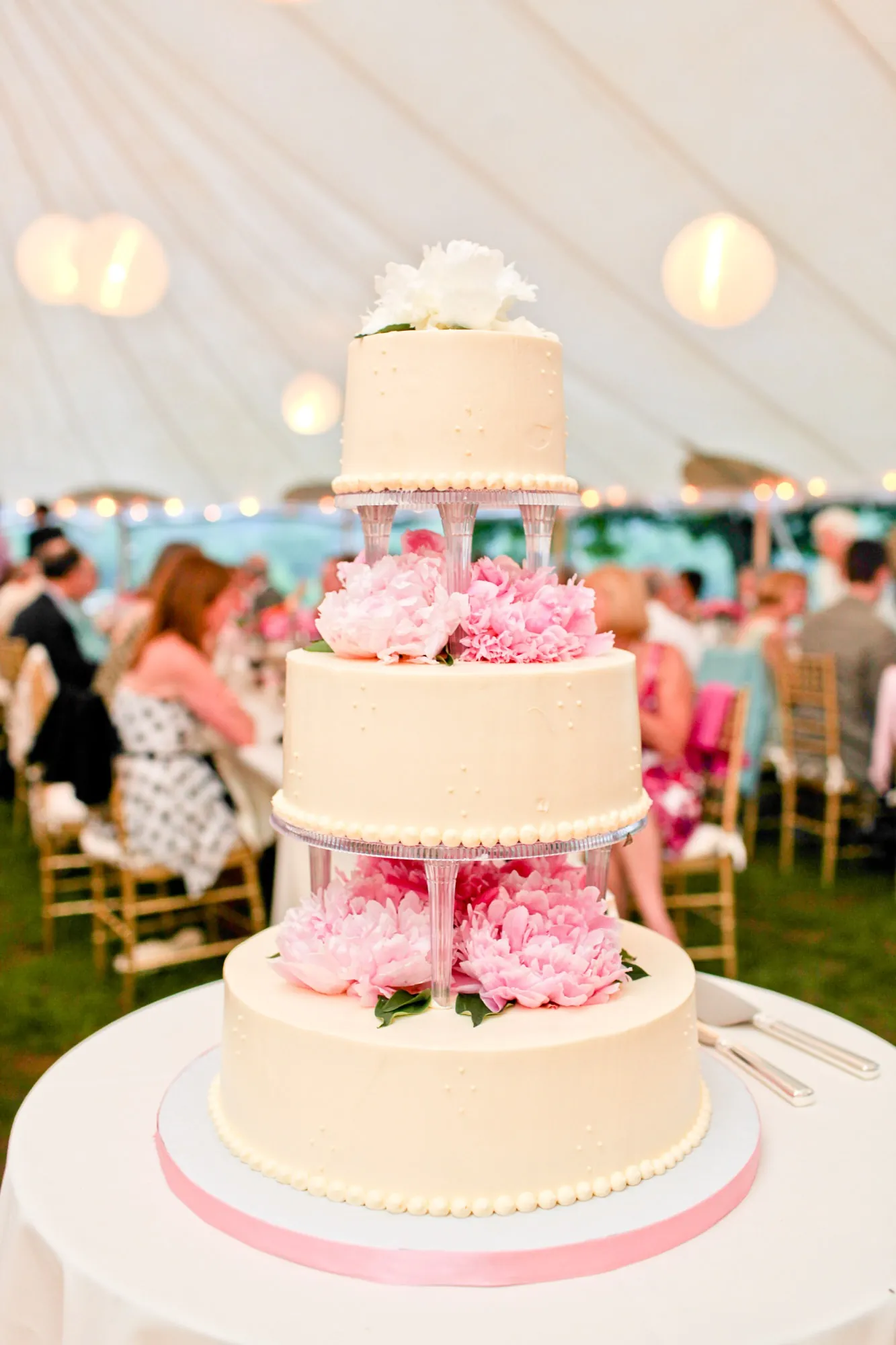 A white tiered cake wrapped in pink flowers under the tent
