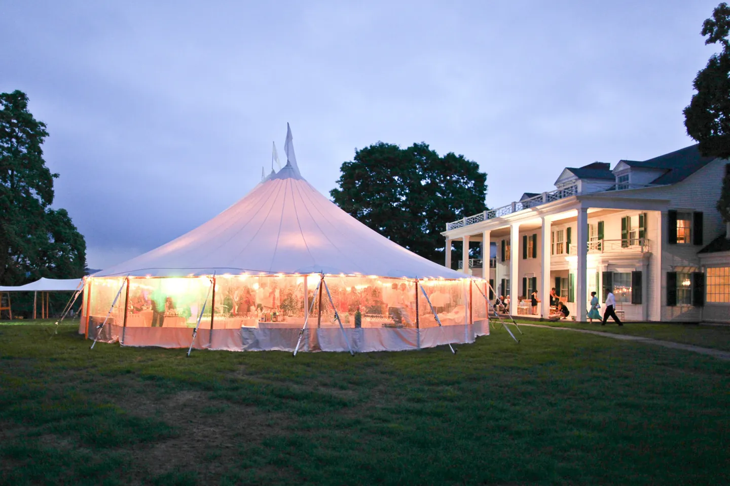 The sailcloth tent glows at blue hour beside the white house