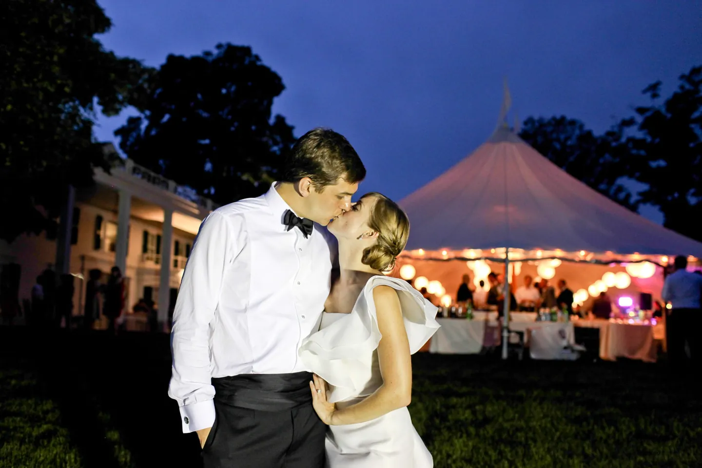 Caity and Matt kiss on the dark lawn with the lit tent behind them