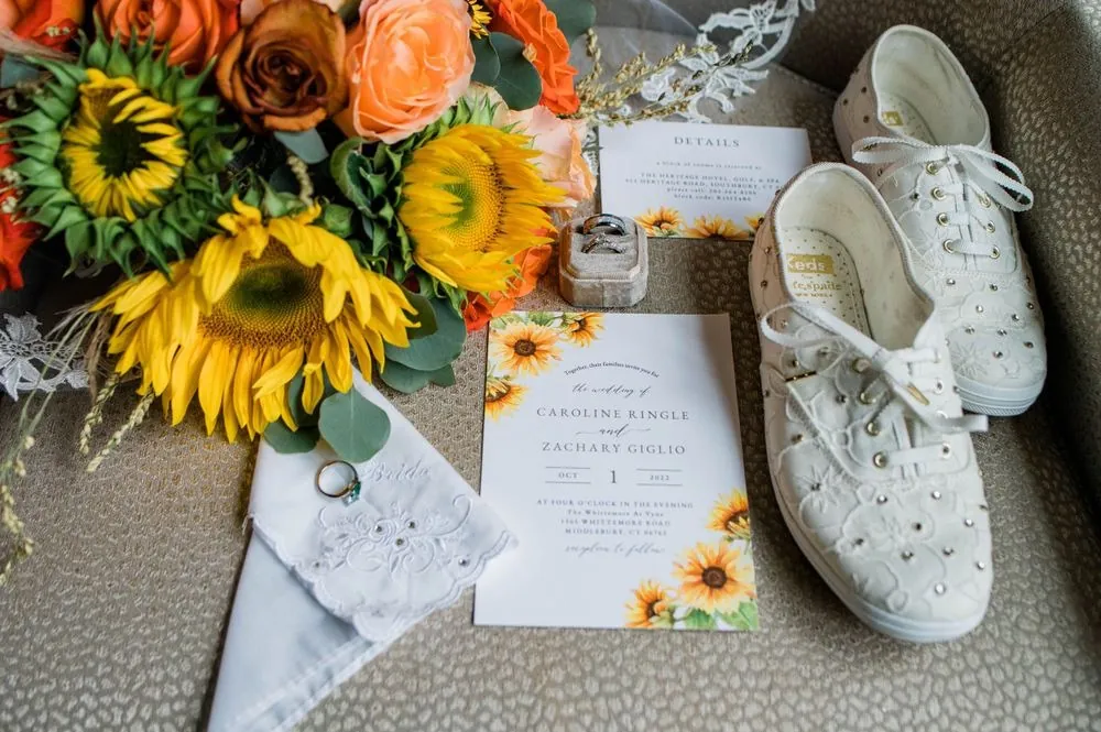 Sunflower and orange rose bouquet beside white sneakers and the invitation suite
