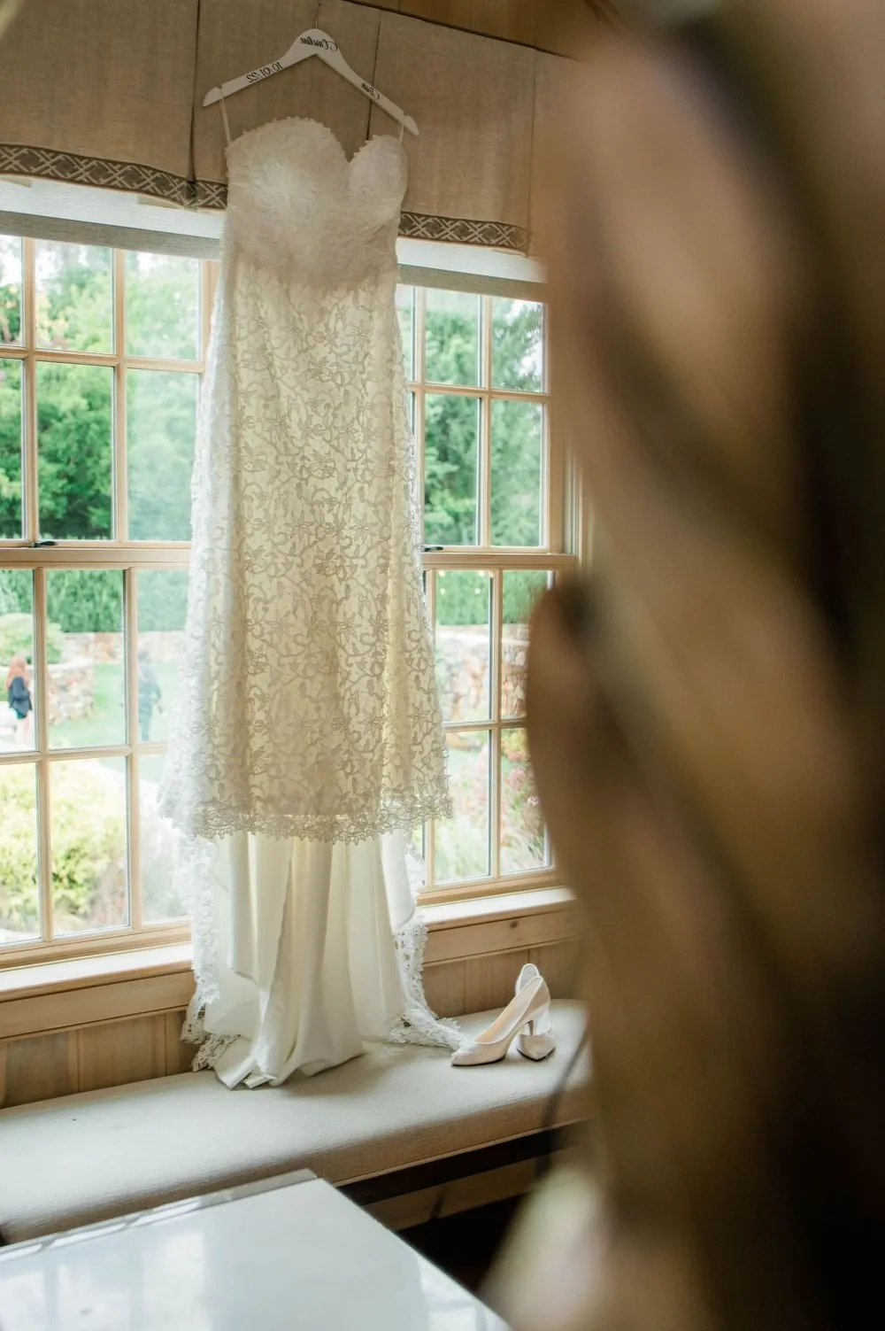 Lace wedding gown hanging near a sunny window in the bridal suite