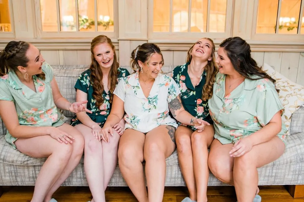 Bridesmaids in floral pajamas laugh together on a couch