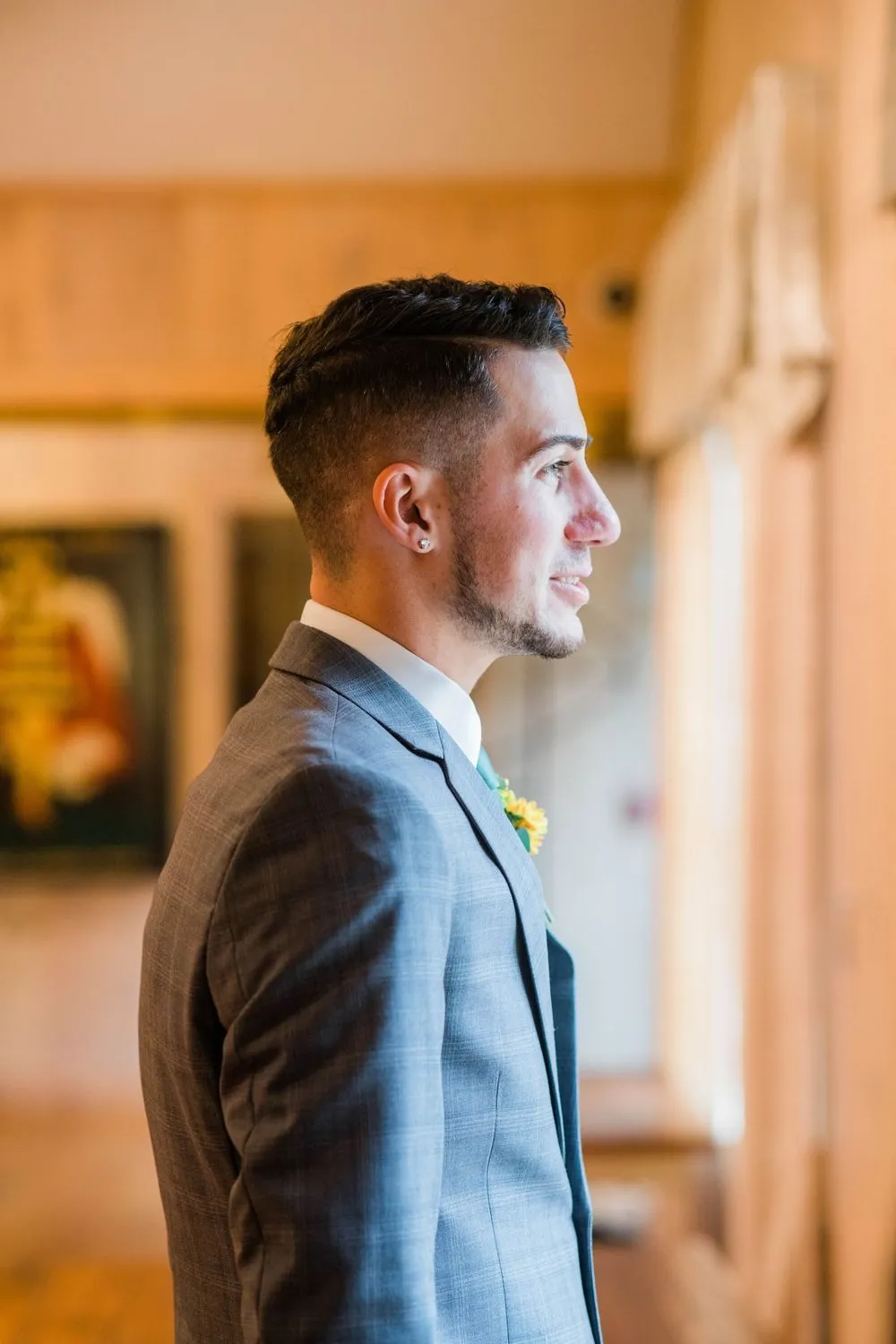 The groom in a gray suit looks toward the window in warm light