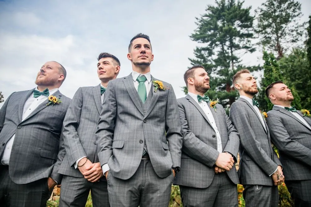 Groomsmen in plaid gray suits and green ties laugh on the lawn