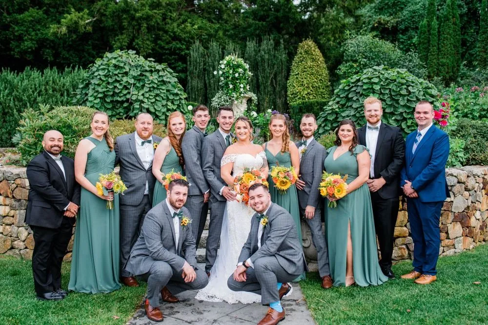 The full wedding party in green gowns and gray suits in the garden