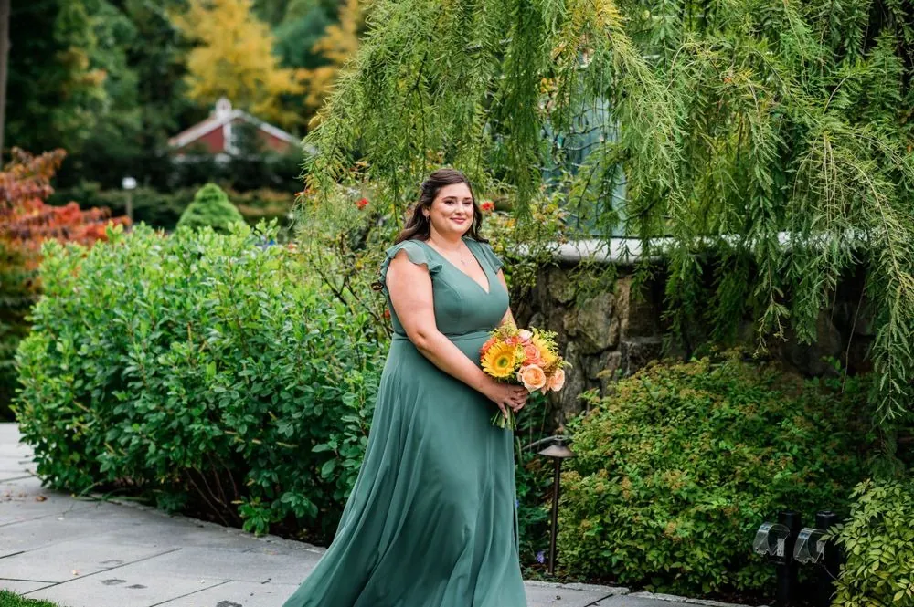 A bridesmaid in a green gown walks the garden path with sunflowers