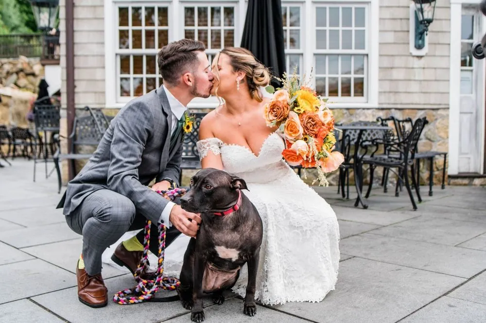 Caroline and Zachary kiss while crouching on the patio with their dark dog