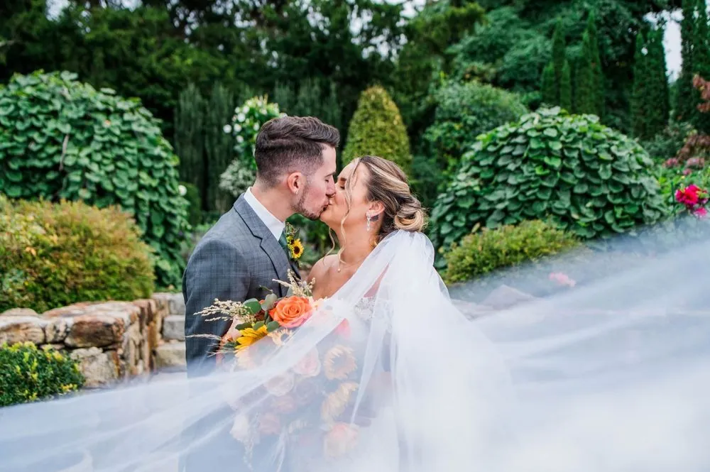Caroline and Zachary kiss in the garden as her veil drifts across the frame