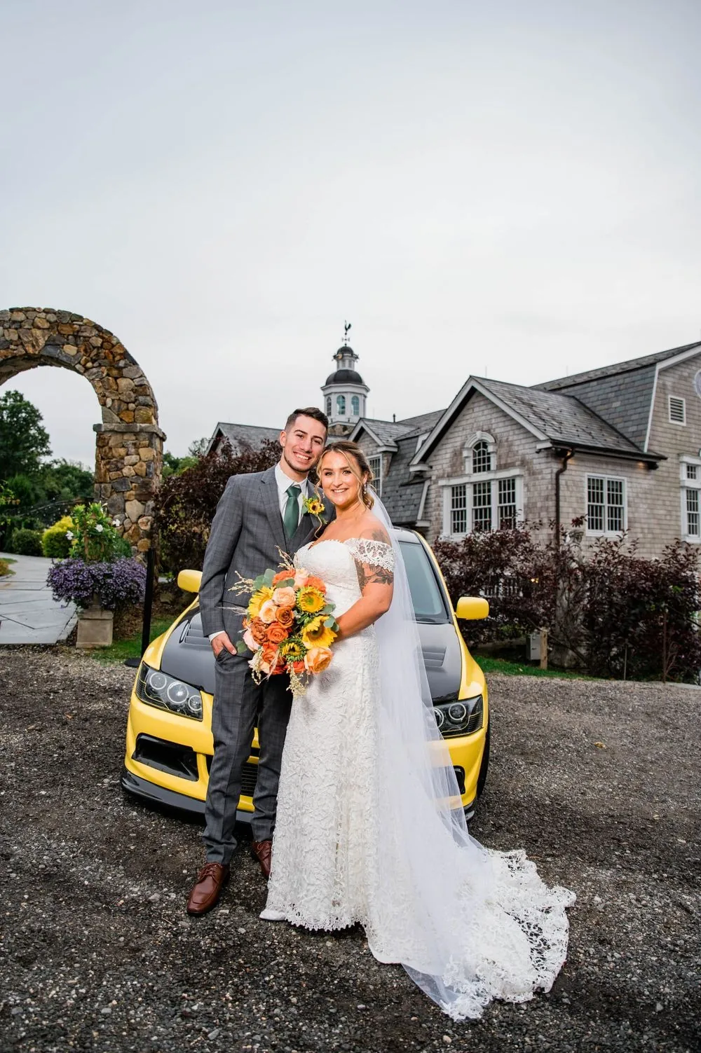 Caroline and Zachary pose with a yellow sports car below the clubhouse cupola