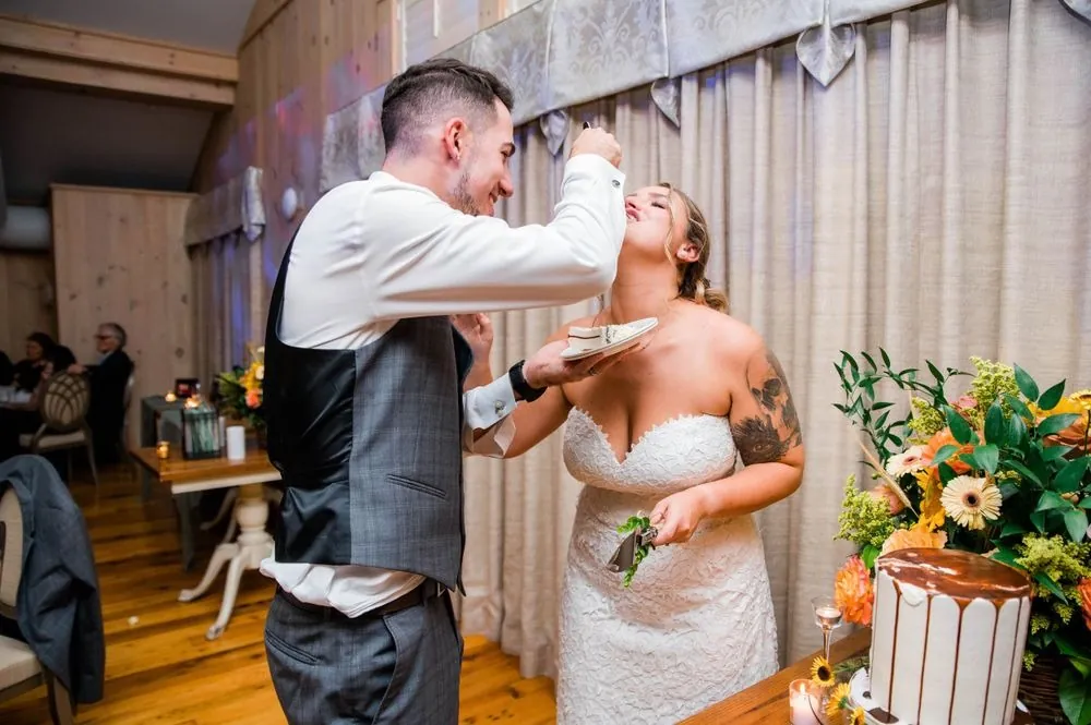 Zachary feeds Caroline cake beside a drip-frosted tier and orange flowers