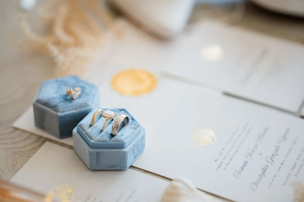 Rings in a pale blue velvet box resting on the wedding invitation with a gold wax seal