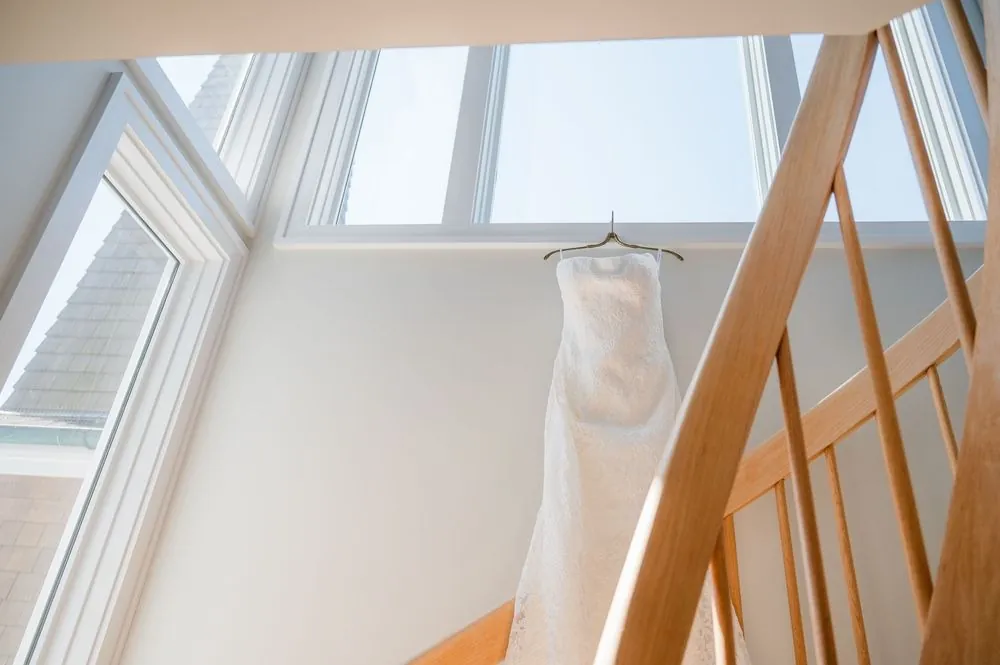 Wedding dress hanging above a pale wood staircase under a wall of bright windows