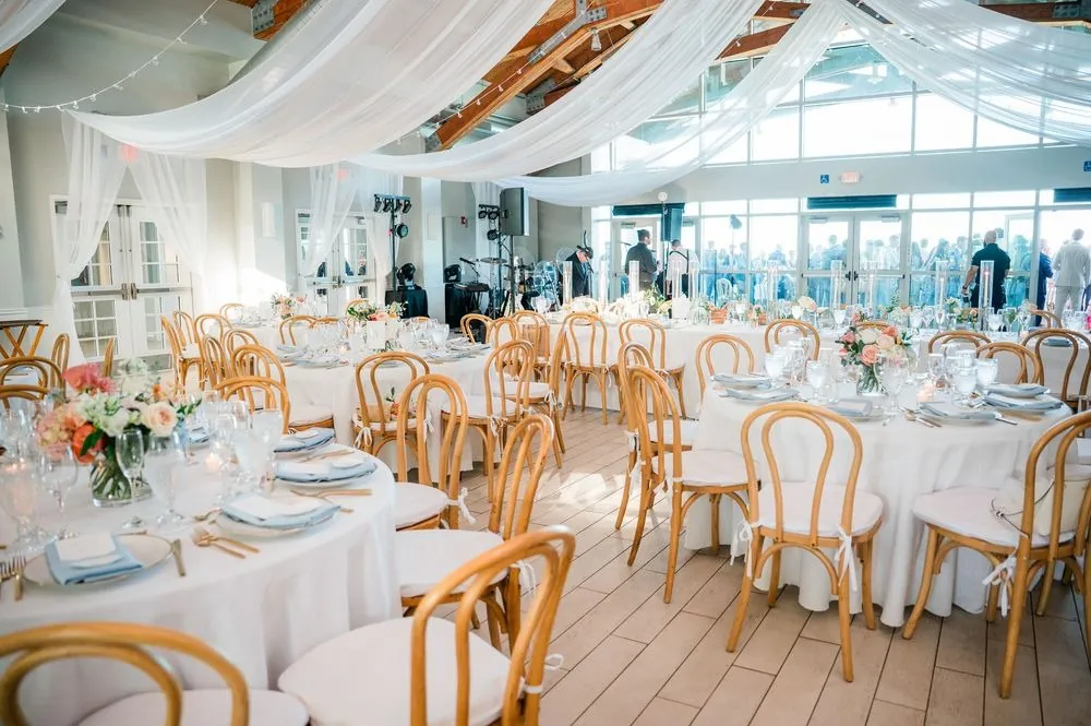 Reception room with gold bentwood chairs, white linens, and sheer draped ceiling fabric