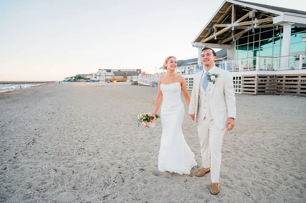 Chris and Carmen walk across the sand toward the camera with the pavilion deck behind them
