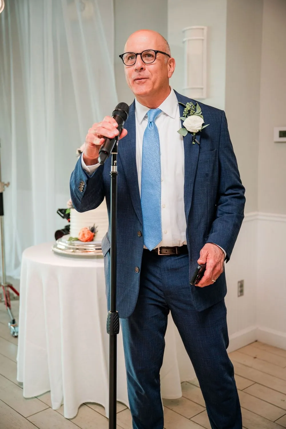 Man in a navy suit and light blue tie gives a toast into a standing microphone