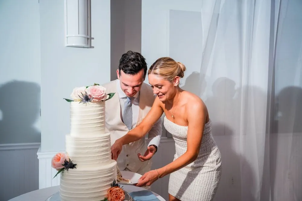 Carmen, now in a short white dress, cuts a tiered white cake with Chris beside her