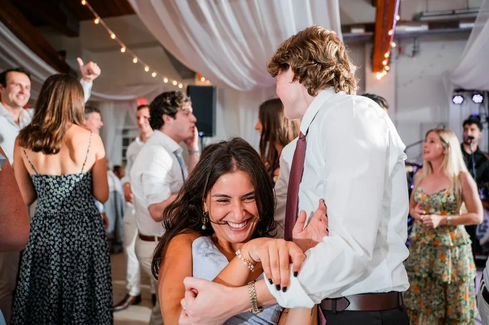 Guests laugh and dance close together on the crowded floor under string lights