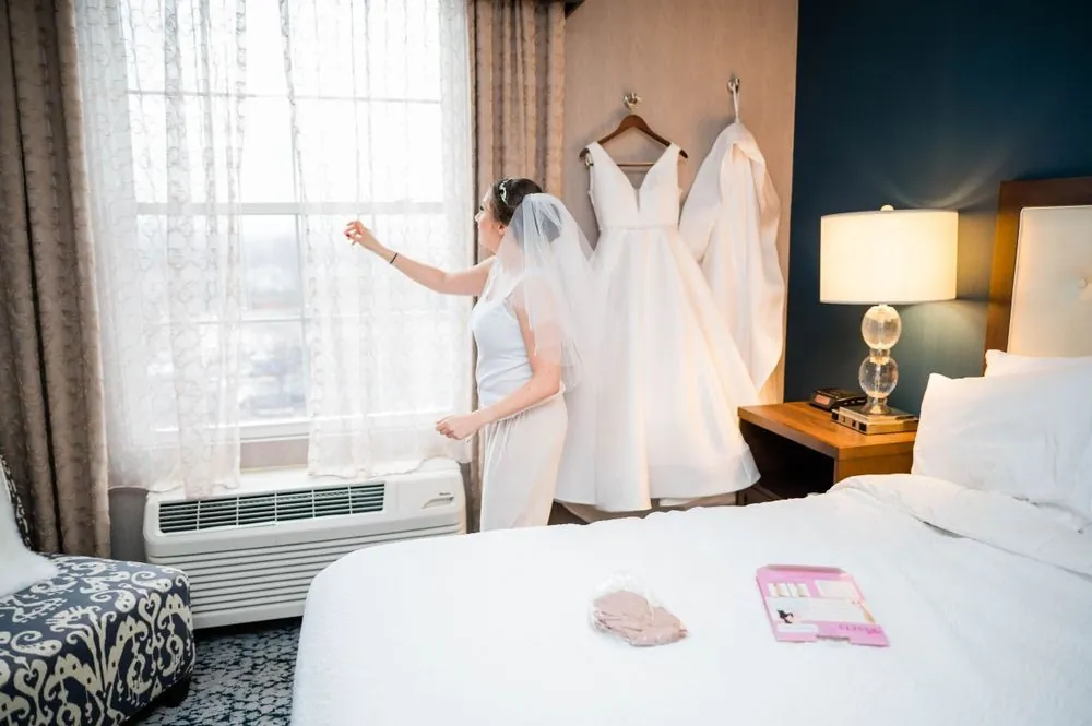 The bride's gown hanging by a hotel window, bridesmaid gowns beside it