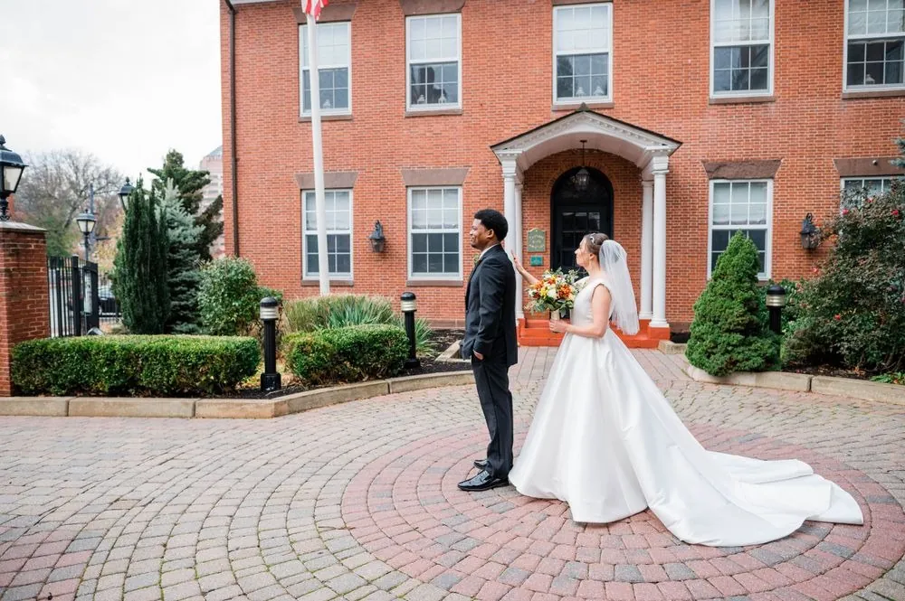 Rebecca taps Claude on the shoulder for their first look in the brick courtyard
