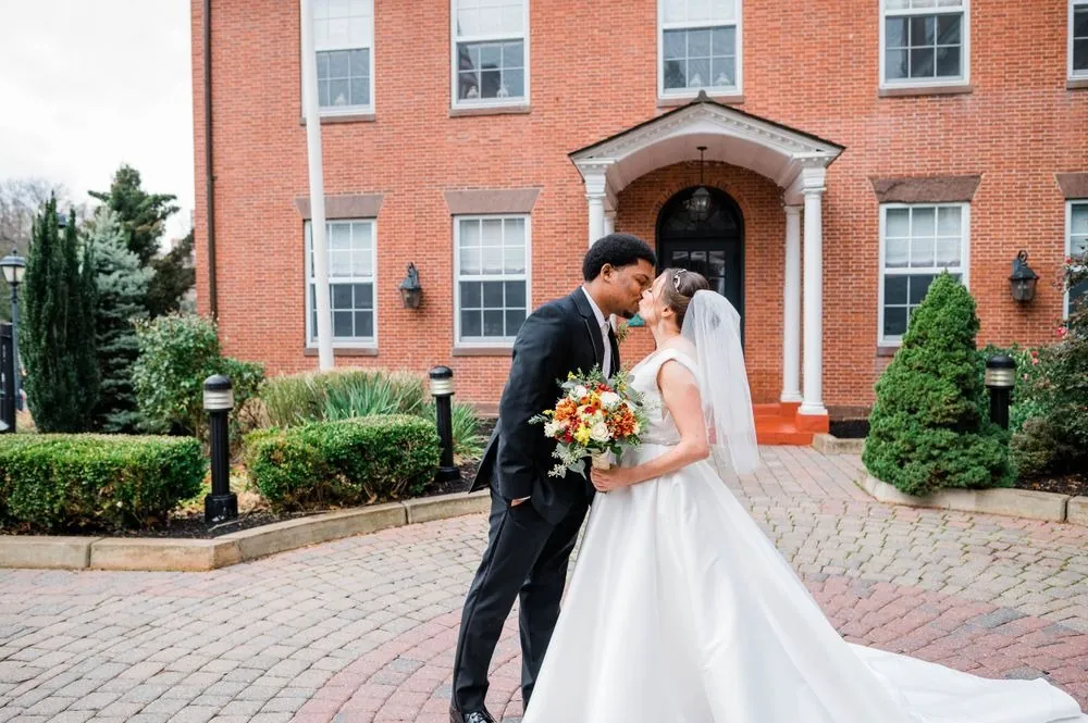 Claude and Rebecca kiss in the courtyard, her long satin train spread across the bricks